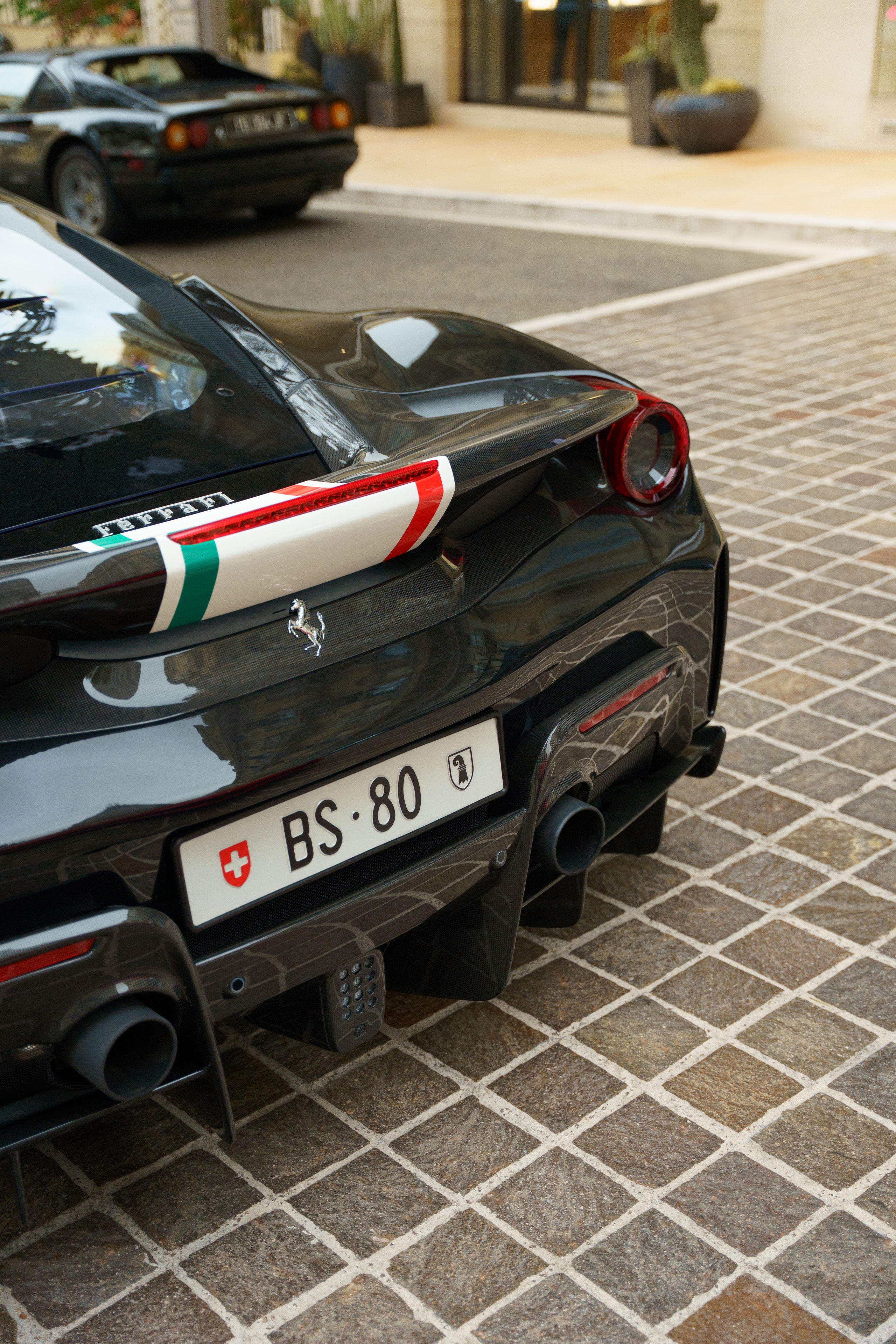 Rear of a black Ferrari with a tricolour stripe, on a paved car park