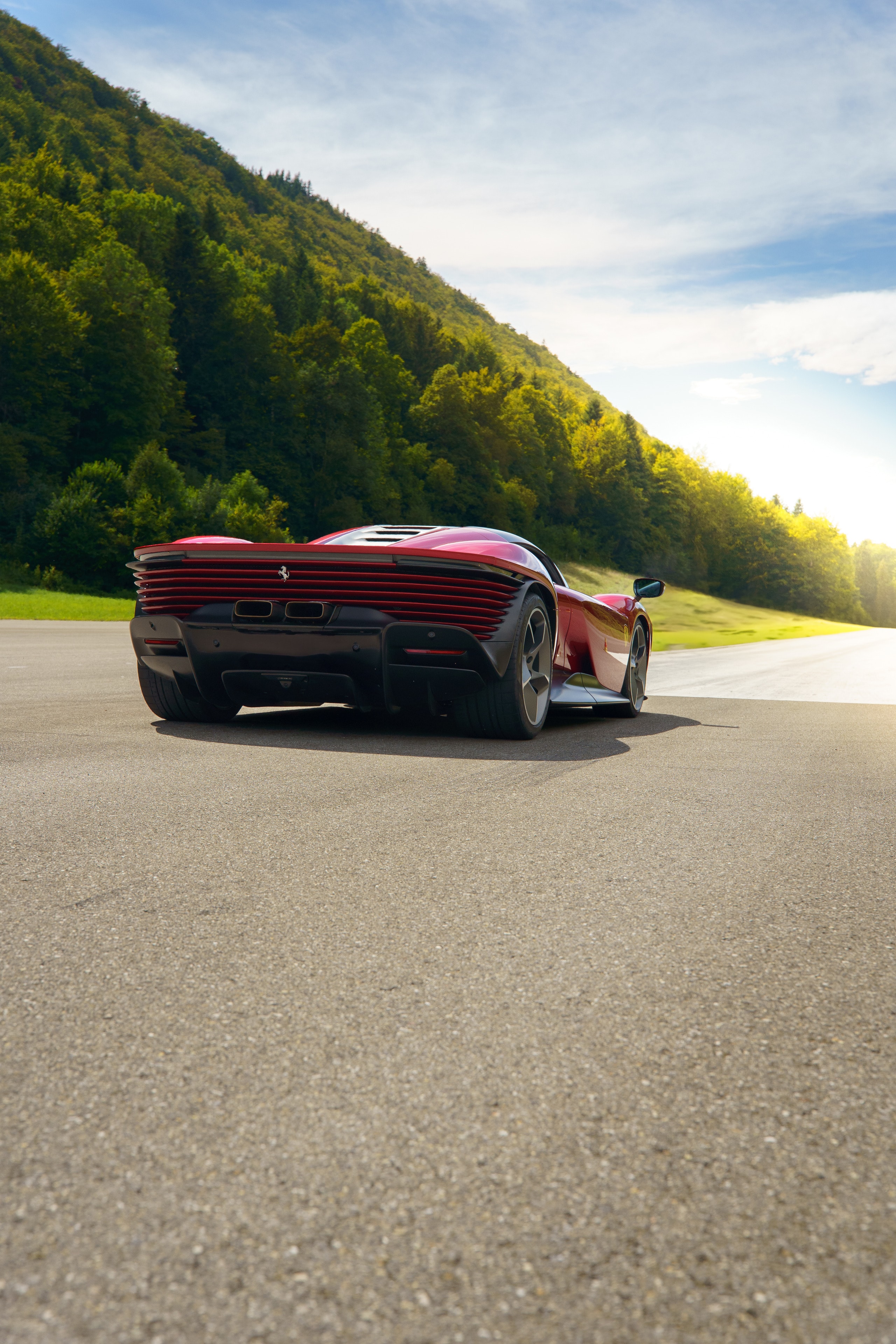 Red Ferrari seen from the rear three-quarter, in full sun in a valley