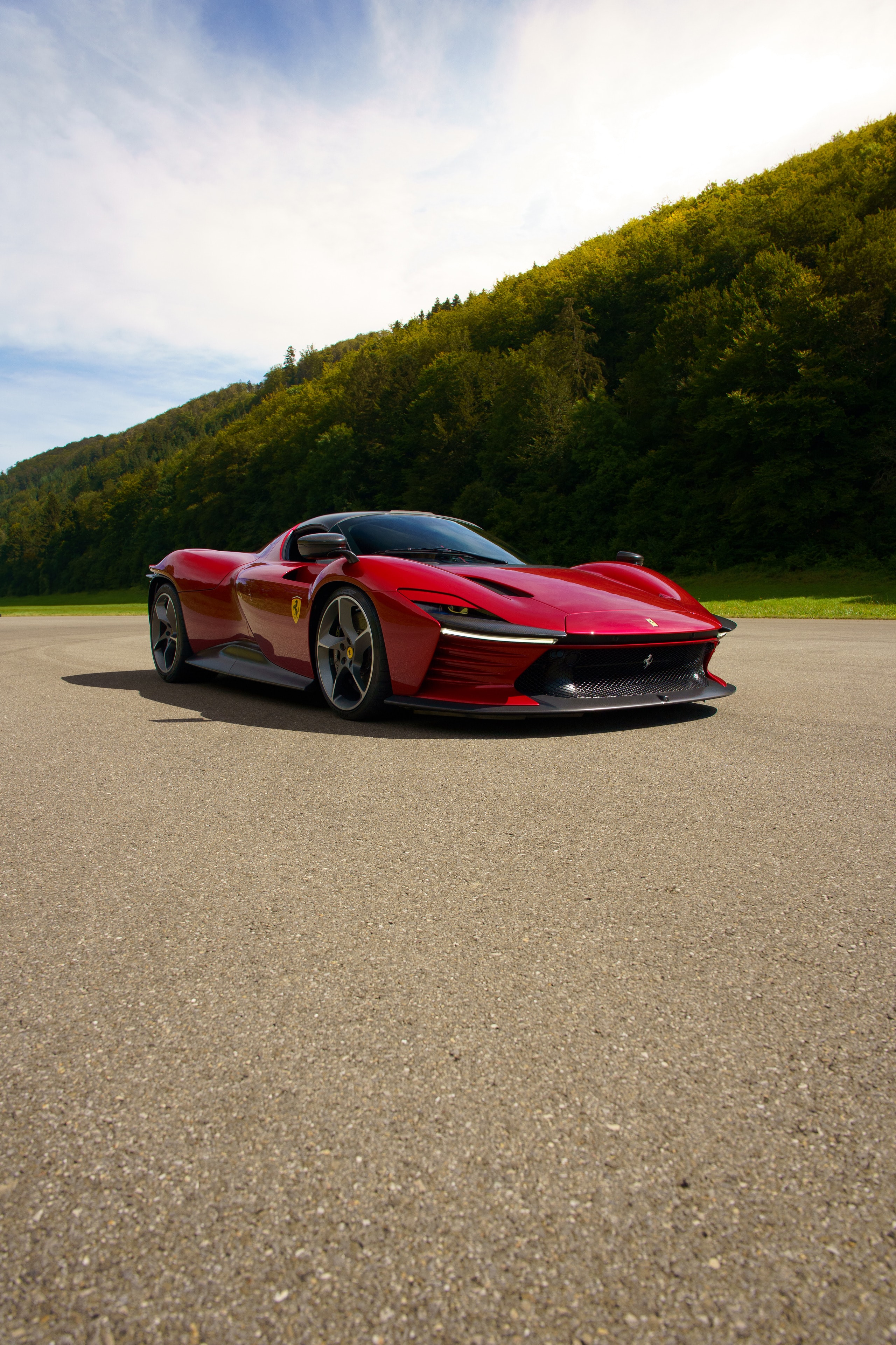 Red Ferrari on a road with wooded hills behind