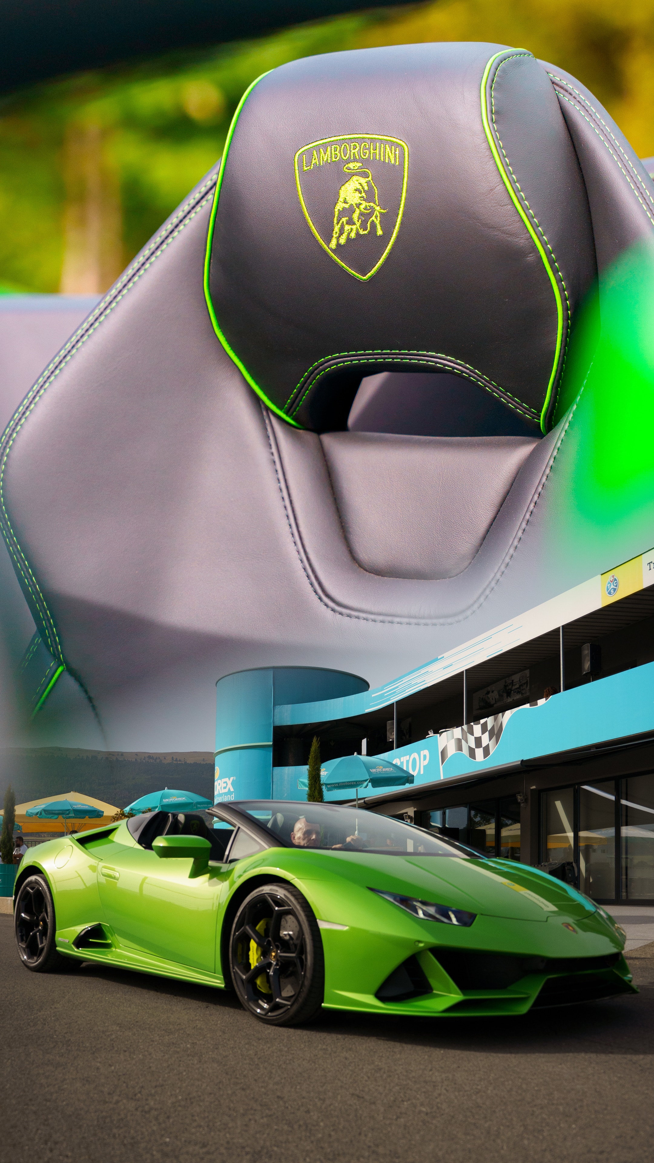 Embroidered Lamborghini seat and a green Huracán in front of a paddock